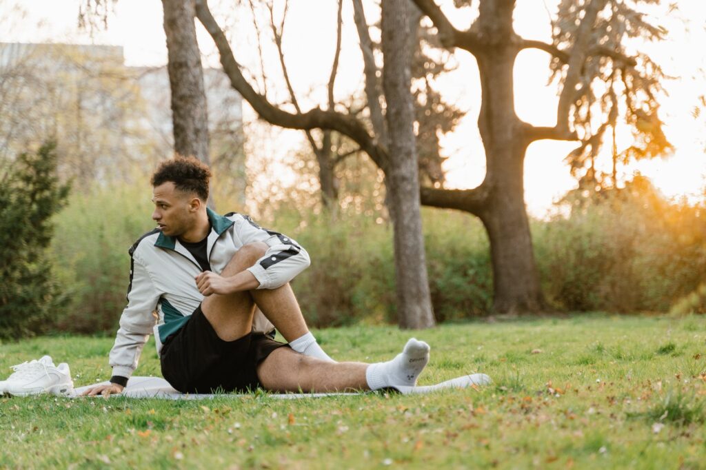 man in white and green jacket stretching on green grass field